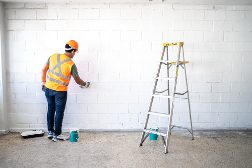 Young painter - construction worker painting a wall indoors