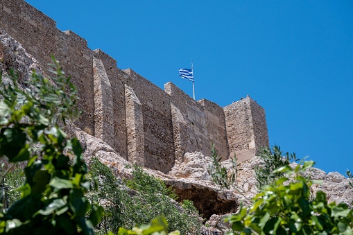 A low angle shot of the walls of Acropolis with a Greek flag waving on the top, Athens, Greece