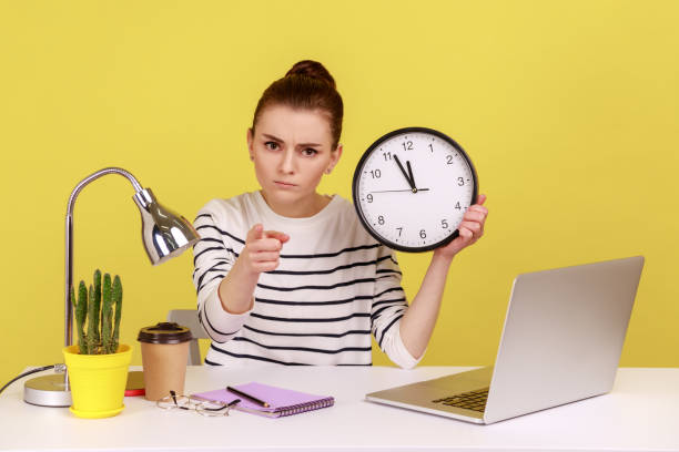 istock Woman worker holding big wall clock, time management, pointing to camera with strict expression. 1436258696