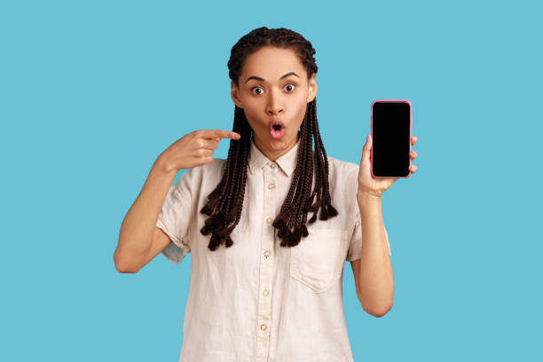 istock Woman with dreadlocks having scared expression, points at phone, demonstrates empty screen of gadget 1436258883