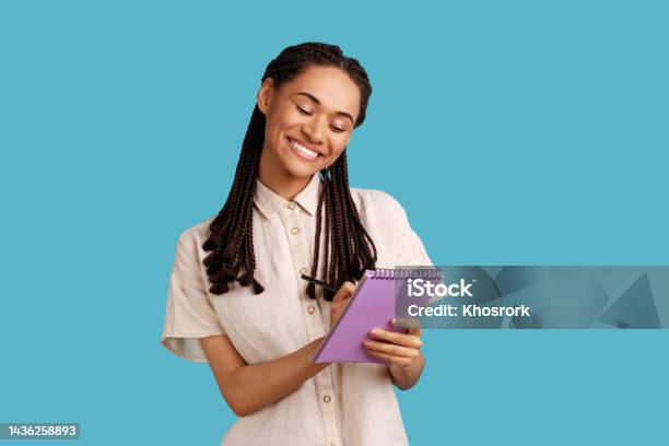 Inspired Woman Smiling And Writing Down Interesting Idea In Notebook Making Plans Todo List Stock Photo - Download Image Now