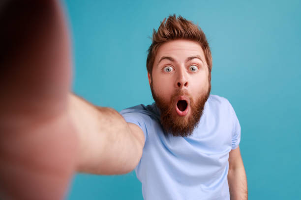 Man standing with widely open mouth, making selfie POV, expressing astonishment.