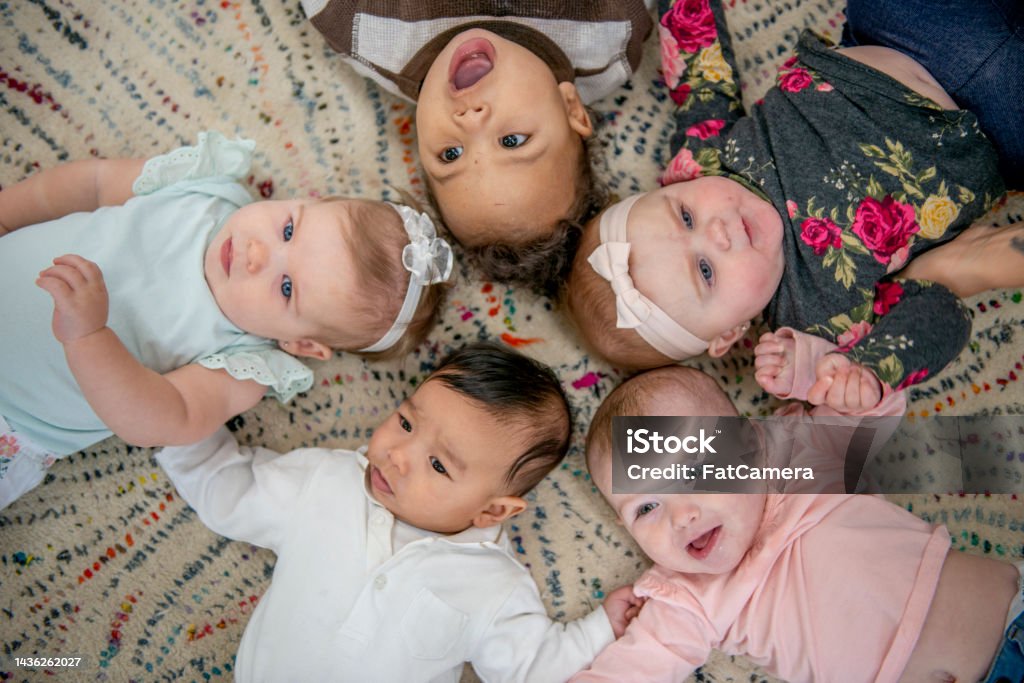 Aerial View of Daycare Children Five babies lay on the floor in a circle with their heads close together as they pose for a portrait.  They are each dressed casually and are smiling in this aerial view photo. Baby - Human Age Stock Photo