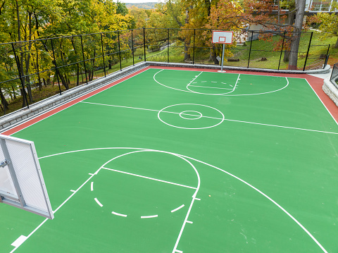 Aerial photo of a green and red outdoor basketball court at school playground.  Court includes retaining walls and black vinyl coated chain link fence.