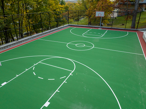 Aerial photo of a green and red outdoor basketball court at school playground.  Court includes retaining walls and black vinyl coated chain link fence.