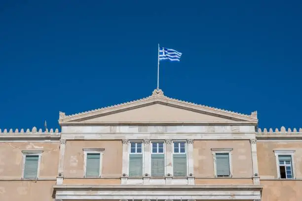 A low angle shot of the Hellenic Parliament and a Greek flag on its rooftop, Athens, Greece