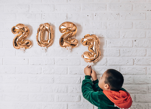 Little boy decorates the wall of the house with golden numbers 2023. concept of the new year