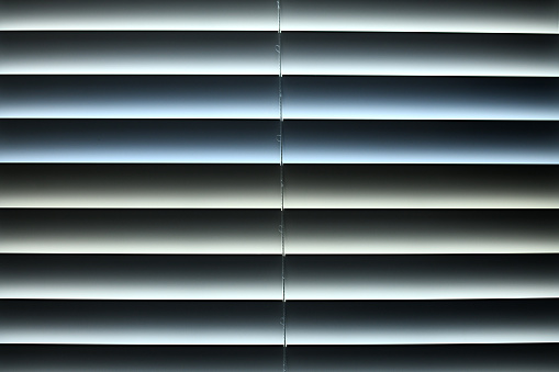 Closed window blinds with the  light outside leaking in with subtle changes in the color of that light