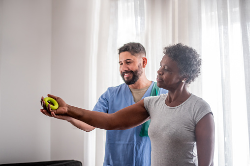 Mature woman doing physical therapy together with male nurse