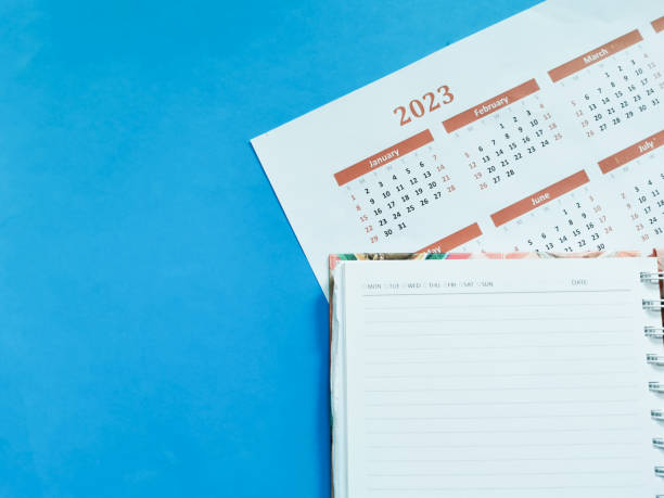 istock 2023 calendar with black note book against blue background. 1436282386