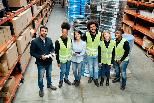 High angle view of diverse workers and supervisors of a distribution warehouse all facing camera smiling cheerfully - Warehouse industry concepts
