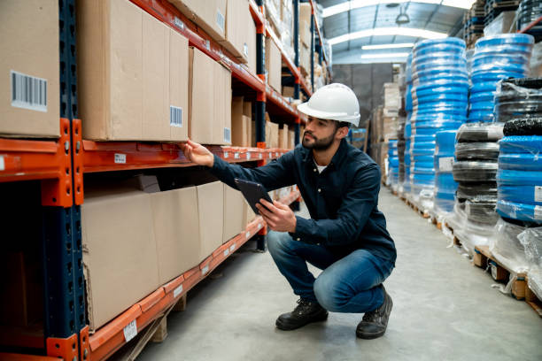 istock Male supervisor working at a distribution warehouse looking for a shipment on storage compartments using a tablet and protective helmet 1436282817