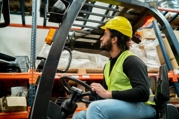 istock Black man working at a distribution warehouse looking at a compartment to place a heavy box using a forklift truck 1436282842