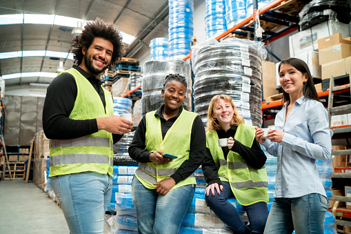 Diverse warehouse workers taking a break drinking a coffee while smiling at camera cheerfully - Industry concepts