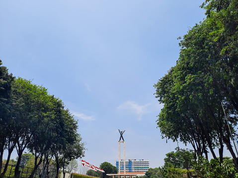 Jakarta, Indonesia - September 25, 2022: View of West Irian Liberation Monument under the blue sky and among the row of trees