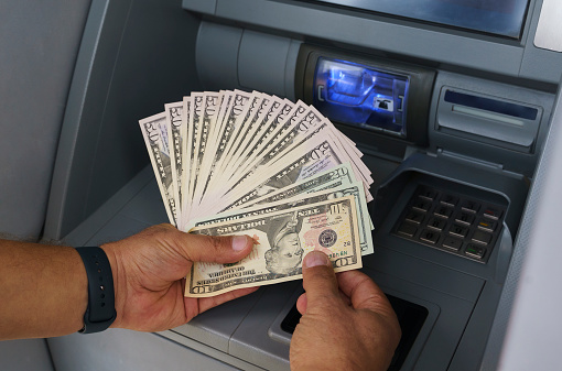 old woman pulls banknotes Israeli shekels from cash withdrawal machine