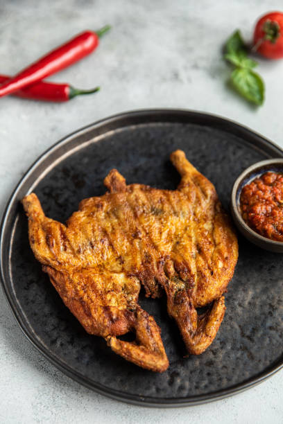 istock Chicken tabaka Dish and tomato with Saltine cracker, chicken tabaka and wings on black table 1436300412