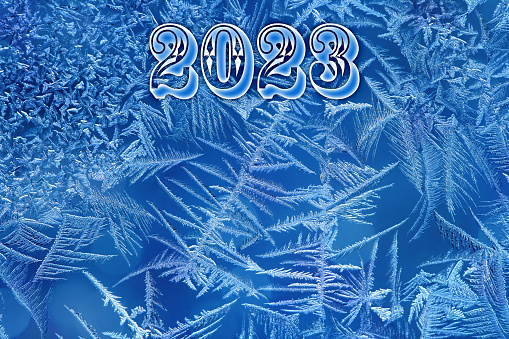New Year 2023 number on a beautiful frost pattern on a window in blue tones.