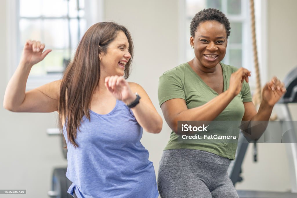 Womens Zumba Class Two mature females bump hips as they participate in a Zumba fitness class.  They are both dressed comfortably in athletic wear and are smiling as they dance their way to fitness goals. 30-34 Years Stock Photo