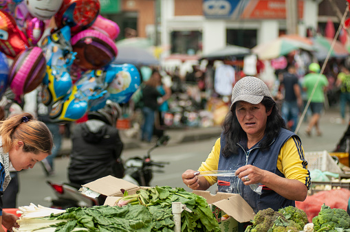 Bogota Colombia 11 de Octubre del 2015\nMujer adulta con gorra quitando vegetales verdes en un mercado callejero