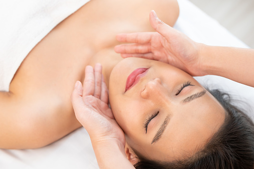 Facial massage treatment. Close-up of a young woman face lying on back, getting face lifting massage in spa salon.