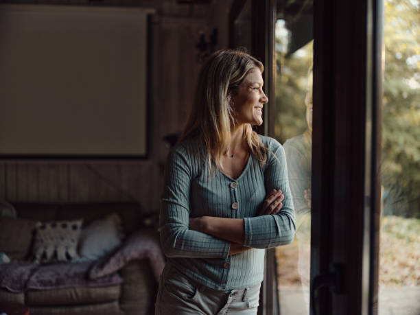 istock Happy woman looking through window from living room. 1436315973