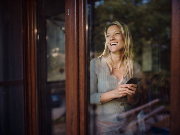 istock Happy woman using mobile phone by the window at home. 1436316326