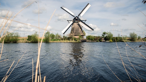 A low-angle shot of a windmill in front of a river with a cloudy sky in the background