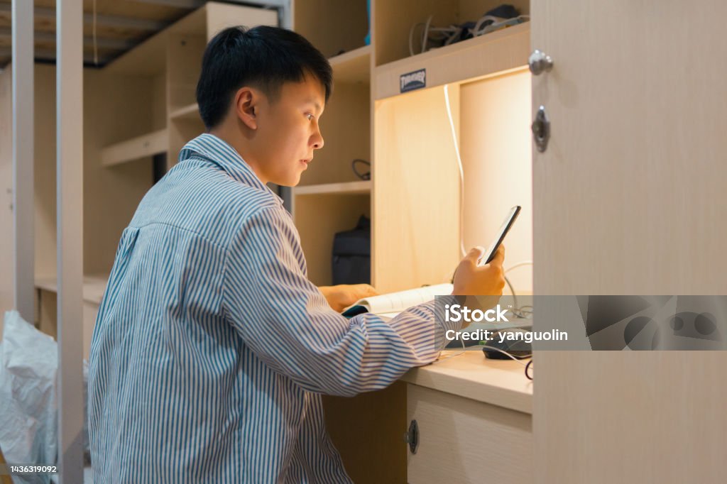 A college student was playing music on his cell phone and reading books in his dorm room 20-24 Years Stock Photo