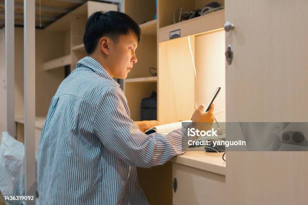 A College Student Was Playing Music On His Cell Phone And Reading Books In His Dorm Room Stock Photo - Download Image Now