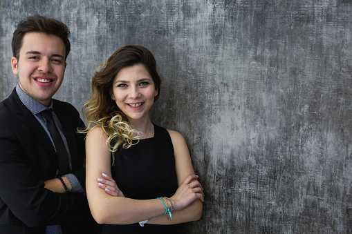 Happy businessman and businesswoman couple standing together posing for a close-up portrait looking at the camera and smiling charmingly. standing in office on gray background