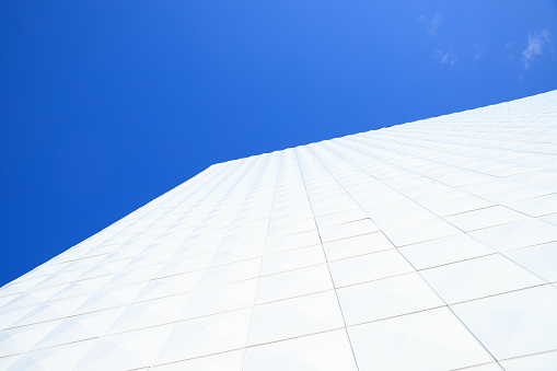 White tiling. View looking up at corner of white generic building facade on blue sky.