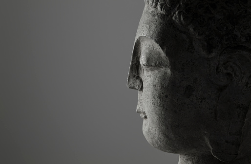 closeup of side view of stone buddha head on white background