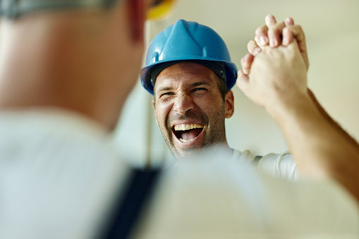 Cheerful manual worker congratulating his colleague at construction site.