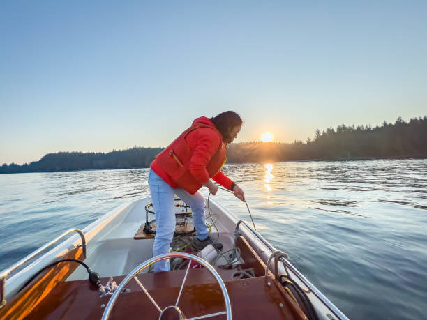 Senior Asian Woman Pulling Crab Trap Up on Boat Woman in 60s checking crab trap early in the morning at sunrise.  Bamfield, Vancouver Island, British Columbia, Canada crabbing stock pictures, royalty-free photos & images