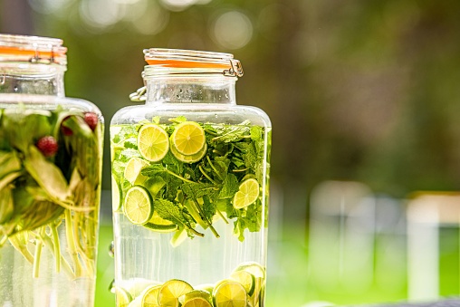 A selective focus of a gallon glass dispenser filled with lemonade with lemons and mint