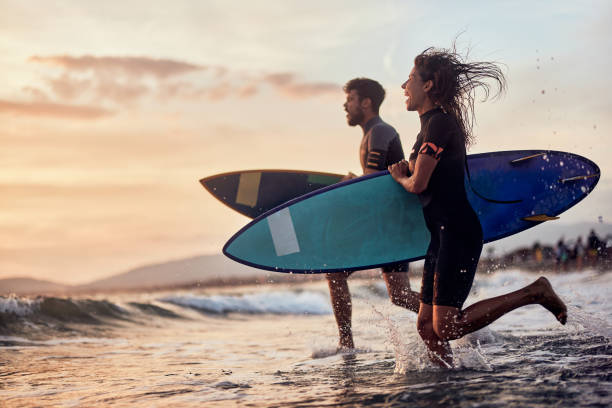 ¡corriendo a surfear al atardecer! - women sea cheerful surfing fotografías e imágenes de stock