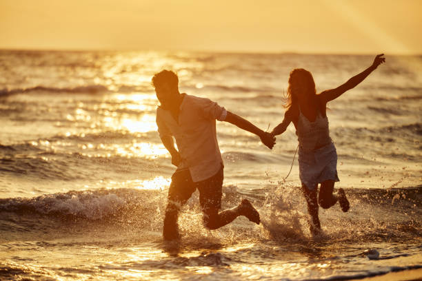 istock Playful couple running through sea on the beach at sunset. 1436332613