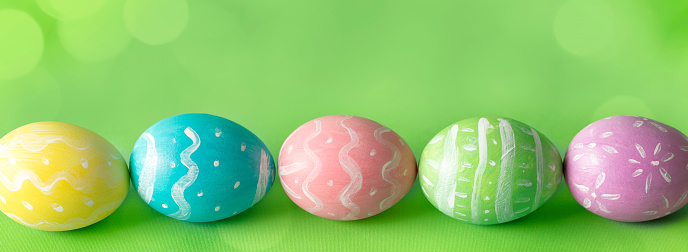 Multi colored hand-painted Easter eggs on a green defocused lights (bokeh) background. Space for copy.