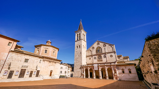 A wide view of the beautiful Duomo in the historic heart of the medieval city of Spoleto, in the Umbria region, central Italy. The Duomo, or Cattedrale di Santa Maria Assunta (Cathedral of Assumption of the Blessed Virgin Mary), was built starting from 1067 in Romanesque and Lombard style and consecrated in 1198. Spoleto, one of the most visited medieval cities in Italy, hosts the Festival of the Two Worlds, a world-famous event that brings together hundreds of artists, musicians, classical dancers and opera singers every year. The Umbria region, considered the green lung of Italy for its wooded mountains, is characterized by a perfect integration between nature and the presence of man, in a context of environmental sustainability and healthy life. In addition to its immense artistic and historical heritage, Umbria is famous for its food and wine production and for the quality of the olive oil produced in these lands. Super wide angle image in 16:9 and high definition format.
