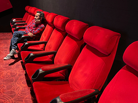 Stock photo showing close-up view of man sitting to watch a film in a cinema whilst eating popcorn from a tub.