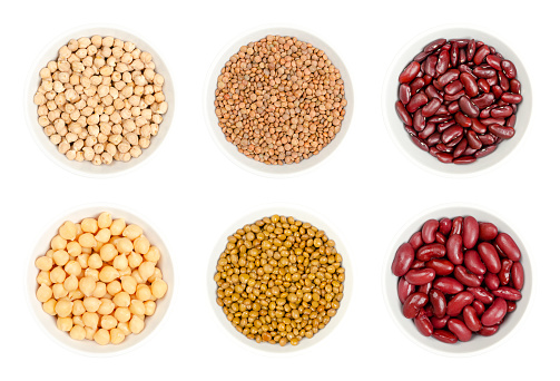 Dried and canned chickpeas, brown lentils and red kidney beans, in white bowls, isolated from above on white background. Raw and cooked seeds of Cicer arietinum, Lens culinaris and Phaseolus vulgaris.