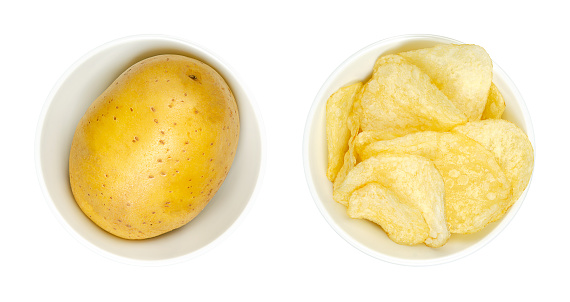 Whole potato and salted potato chips, in white bowls, from above, isolated, on white background. Raw potato, a tuber of root vegetable Solanum tuberosum, and crisps, slim slices of deep fried potato.