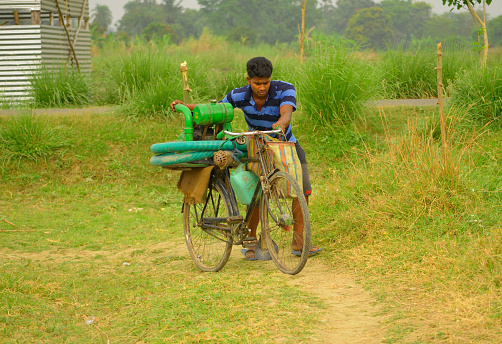 Hooghly, India - April 09, 2017: A man carrying water pump in his cycle through the village road.