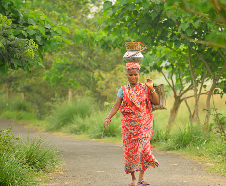 Hooghly, India - April 09, 2017:  A woman walking along a road carrying a pot in her head.