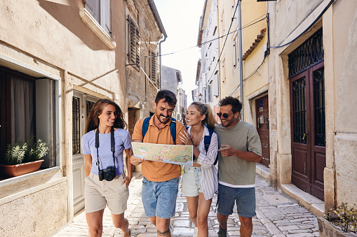 Young happy couples of tourists examining a map while walking on the city street.