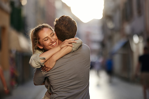 Happy woman enjoying in a hug with her boyfriend on the city street.