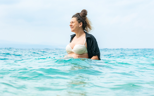 The pregnant woman stands in sea water and admires the seascape. The pregnant woman spends her maternity leave at a seaside resort. Adriatic Sea. Croatia.