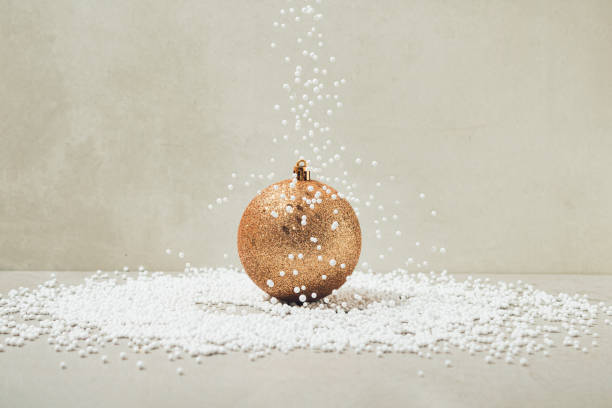 Artificial snow falling on golden colored shiny Christmas bauble. Minimal holiday greeting concept.