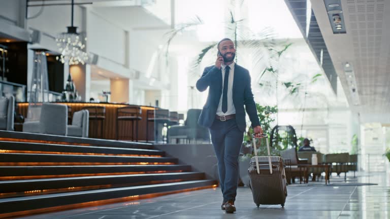 Business, travel and work phone call of a black man executive walking in a hotel. Businessman, corporate and working employee with a suitcase talking and speaking using technology